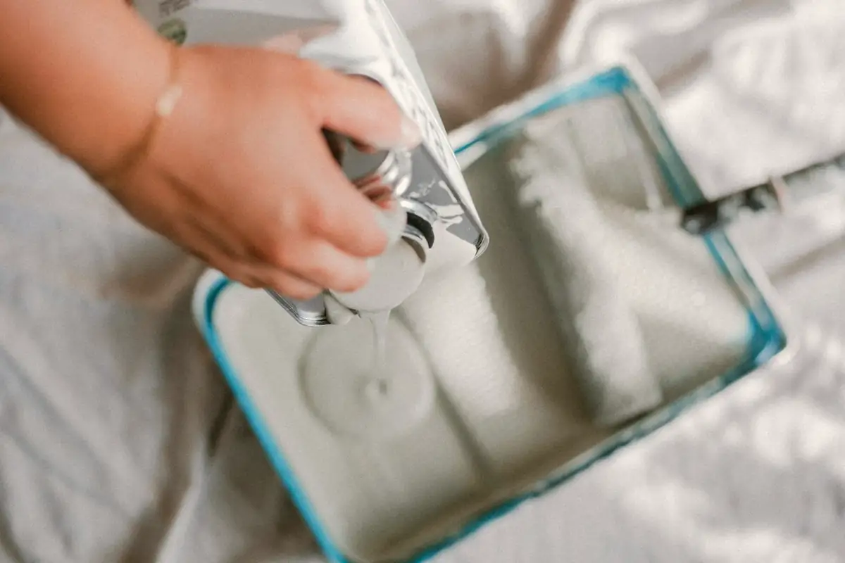 Peinture blanche versée dans un bac à rouleau posé sur une bâche