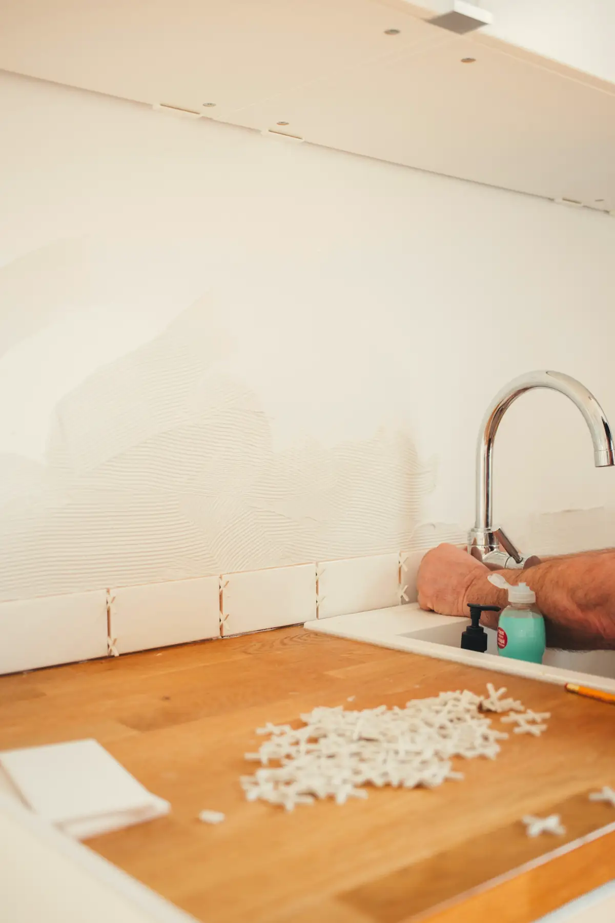 Croisillons de carreleur éparpillés sur un plan de travail en bois, faïence blanche au mur