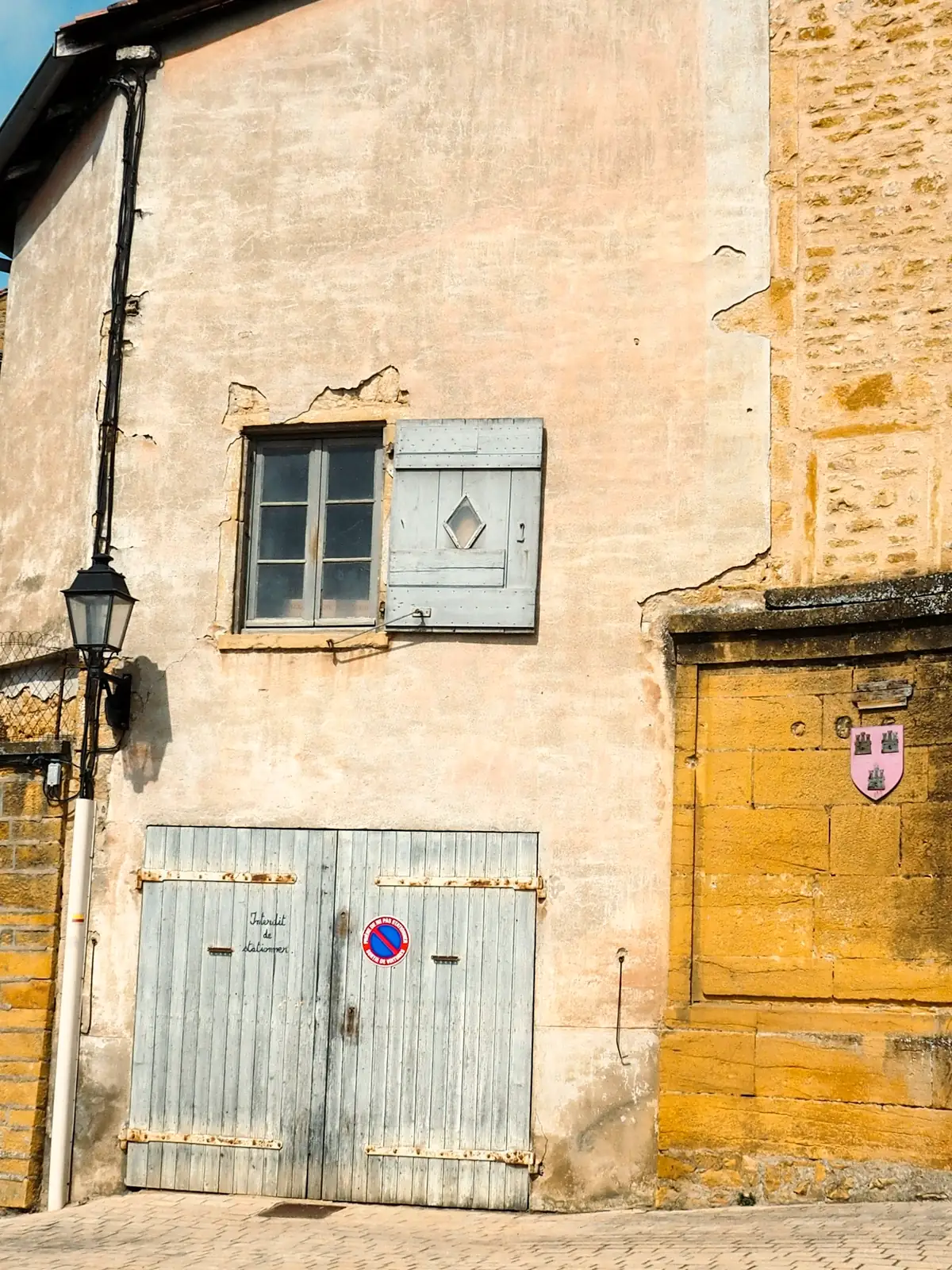 Façade ancienne aux enduits repris par endroits, portes de grange et volet gris
