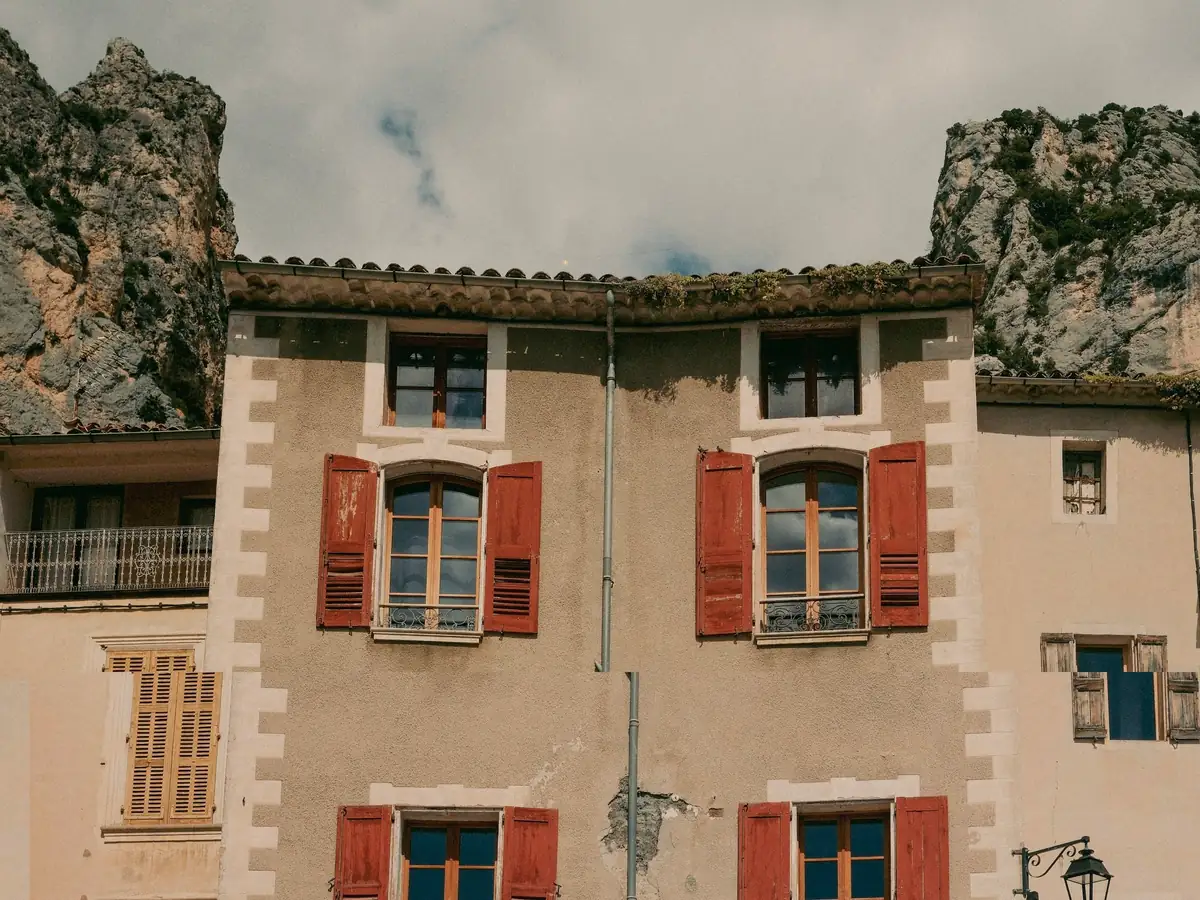 Façades enduites à encadrements clairs et volets rouges, au pied de falaises