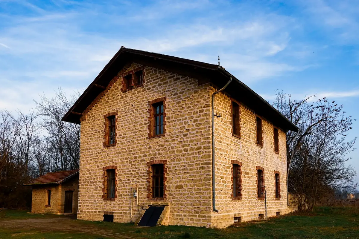 Maison à étage en pierre blonde appareillée, fenêtres à volets et toit de tuiles