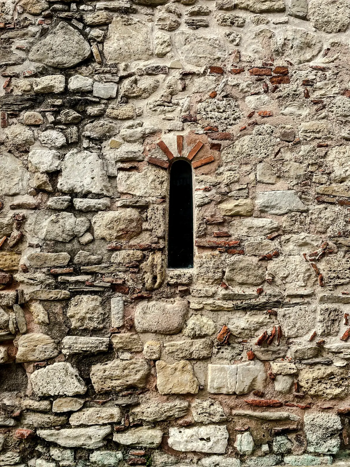 Mur ancien de moellons percé d’une étroite ouverture cintrée