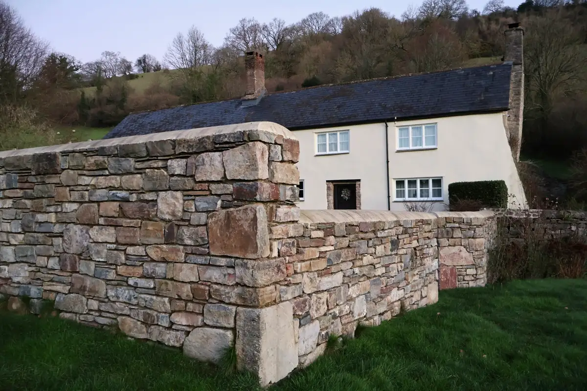 Murs de pierre montés au mortier devant une maison blanche, à flanc de colline