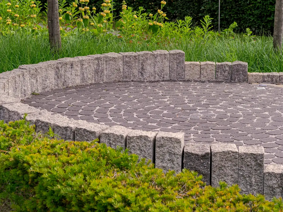Terrasse ronde pavée en éventail, bordée de pierres debout et de massifs