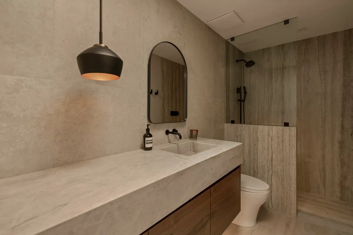 Salle de bain en grands carreaux couleur pierre, plan vasque et douche vitrée
