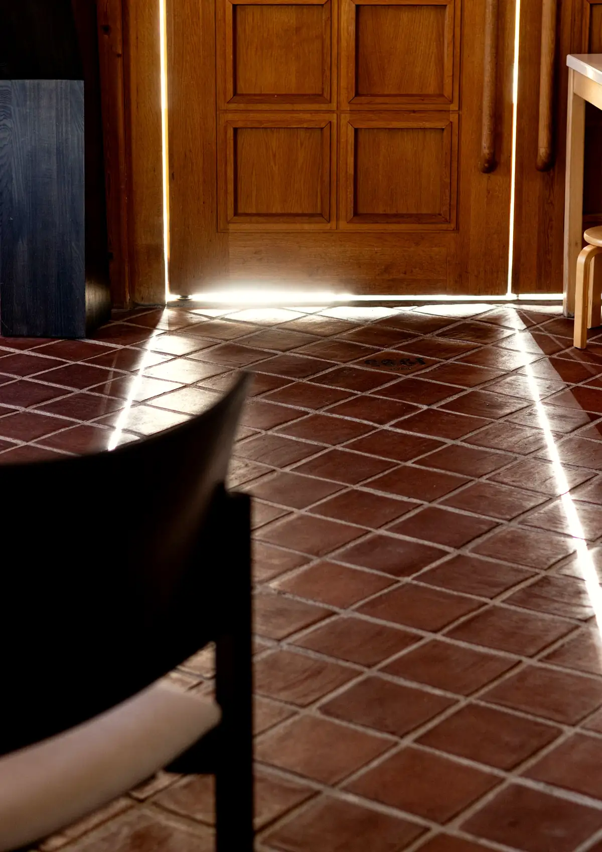 Sol de carreaux de terre cuite traversé par la lumière d’une porte entrouverte